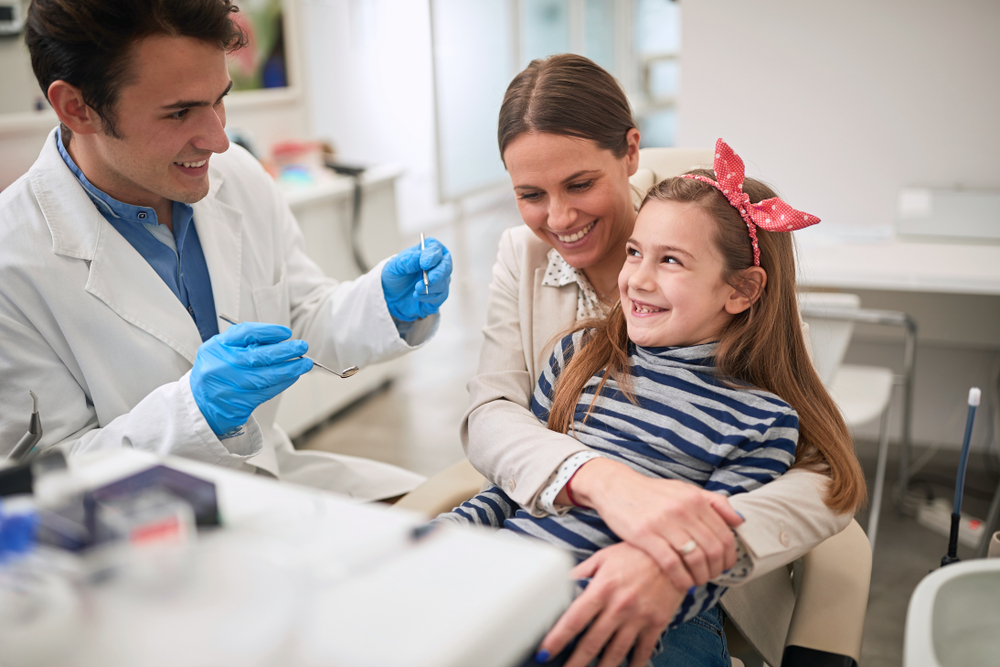 Family,in,dentists,office.dentist,examining,his,smiling,girl,patient,in